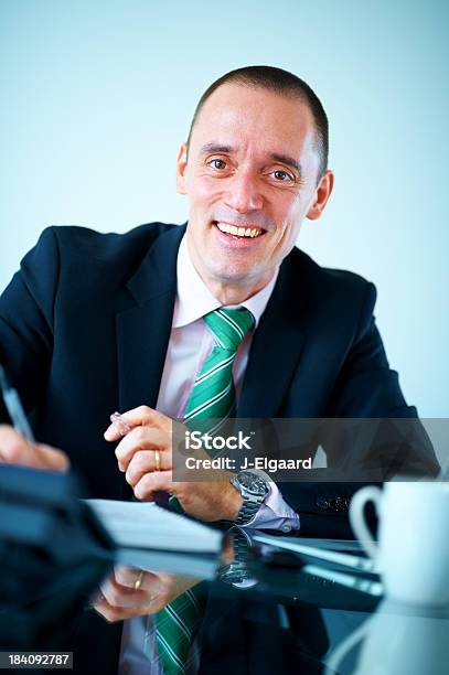 Elegante Hombre De Negocios Sonriendo Mientras Escribir Notas En Oficina Foto de stock y más banco de imágenes de Adulto