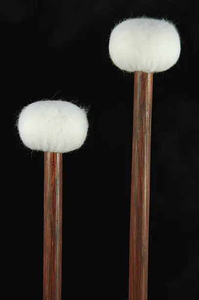 A pair of new orchestral timpani (kettledrum) mallets against a black background.