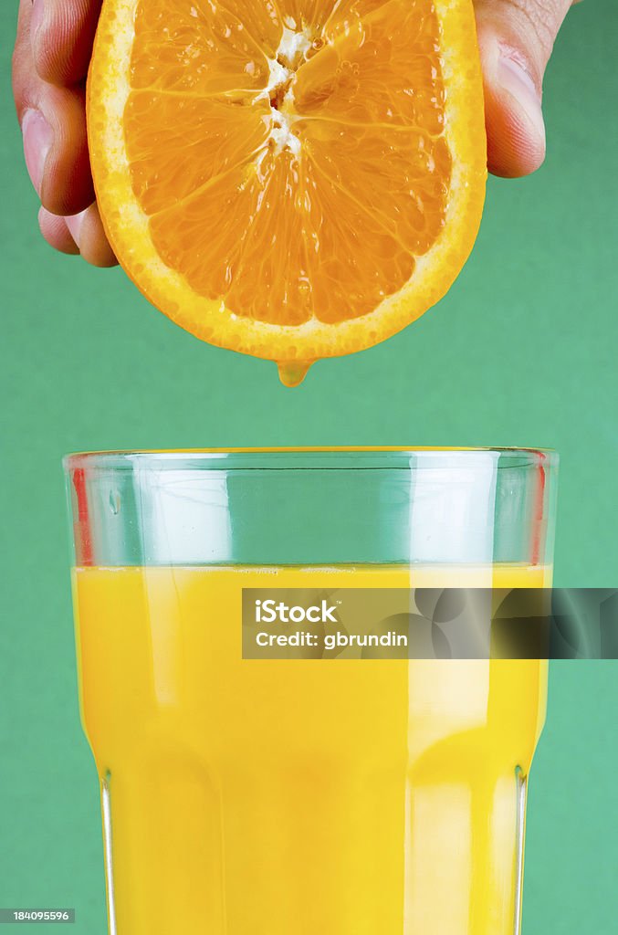 Squeeze it! Juice from an orange dripping down in a filled glass of orange juice. Orange Juice Stock Photo