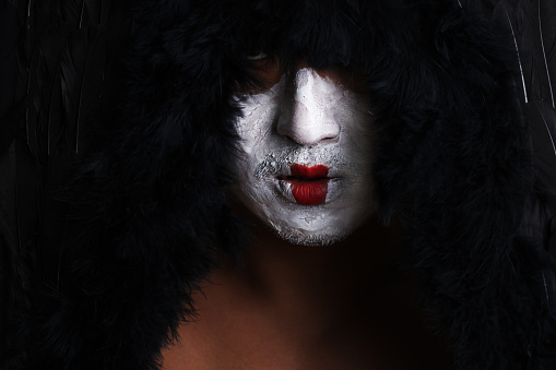 Asian man surrounded in black feathers with patchy painted face