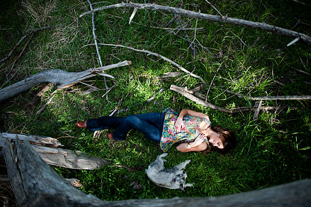 Looking down on a beautiful young woman lying in the grass next her cute little puppy.