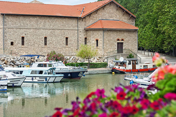 Canal Du Midi: The port of Colombiers "The small town Colombiers is a very popular port of the Canal Du Midi (World Heritage). In the near the towns Beziers and Narbonne. View onto the harbour basin with some small boats. Selective focus with blurred flowers in the foreground. Colombiers, Herault, Languedoc-Roussillon, France." beziers stock pictures, royalty-free photos & images