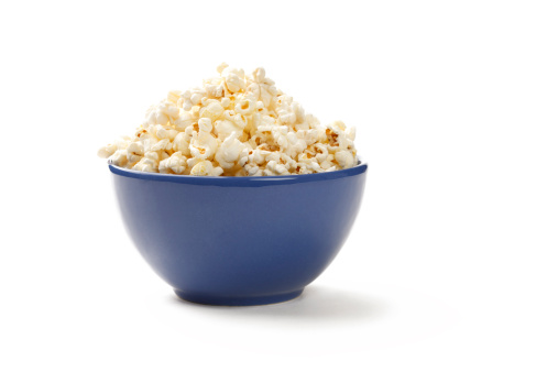 Fresh popcorn spilled from a cardboard striped cup on a blue wooden background with copy space. Top view.