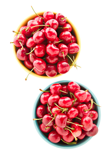 A close up overhead view of two bowls full of ripe red cherries. Isolated on white.