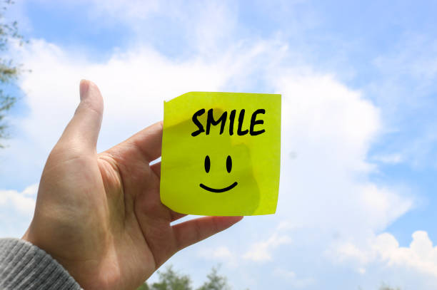 istock Hand holding note writing SMILE smile emoji with blue sky and clouds background. Motivational word wallpaper SMILE written on sticky note 1840991689