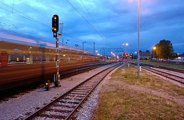 "Ljubljana railway station by dusk and train passing by, creating motion blur effect."