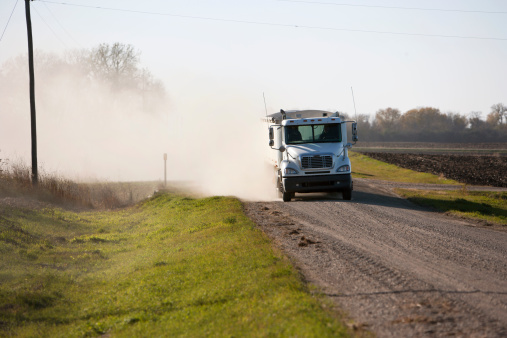 Truck hauling grain on dusty Midwest Road.