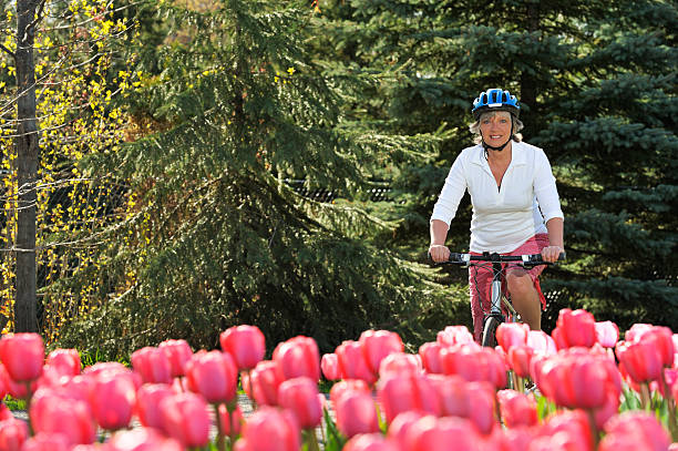 lächelnde frau fahrradfahren in der nähe der rosa blumen garten - bicycle ornamental garden flower formal garden stock-fotos und bilder