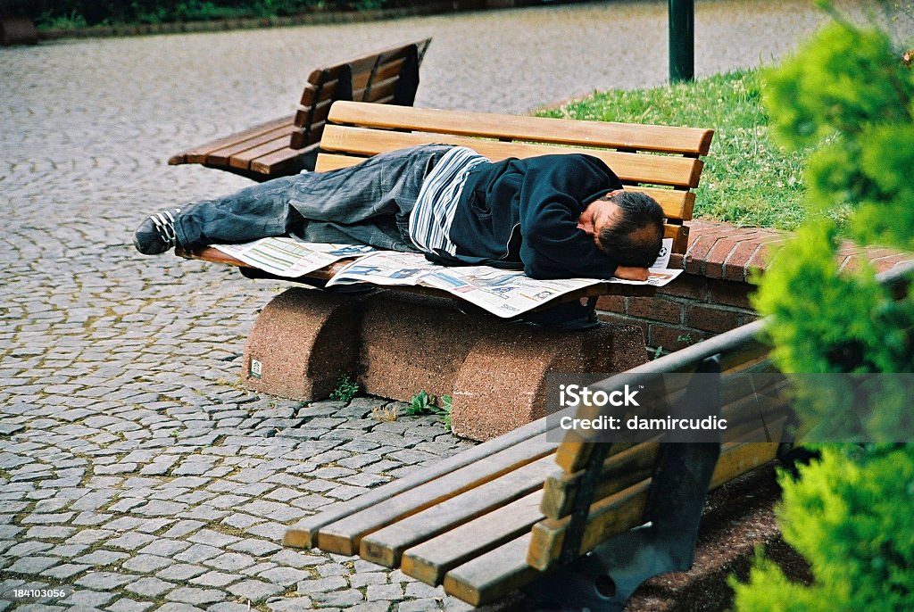 Senzatetto uomo di dormire su una panchina nel parco - Foto stock royalty-free di Senzatetto