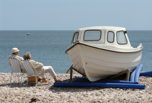 An elderly couple relax in folding chairs next to a beached boat