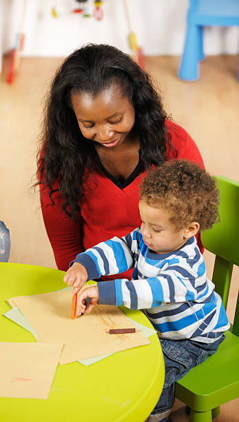 istock Carer Watches Creative Toddler Doing Artwork In A Nursery Setting 184104354