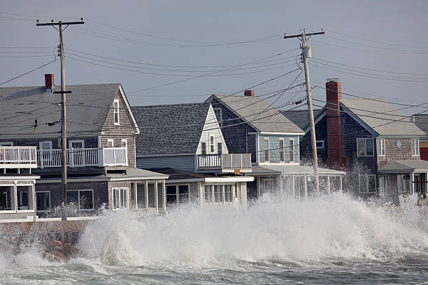 Ocean Storm Waves Crashing into Seawall in front of Houses Waves crash against a break wall in conjunction with high tide and a storm. high tide stock pictures, royalty-free photos & images