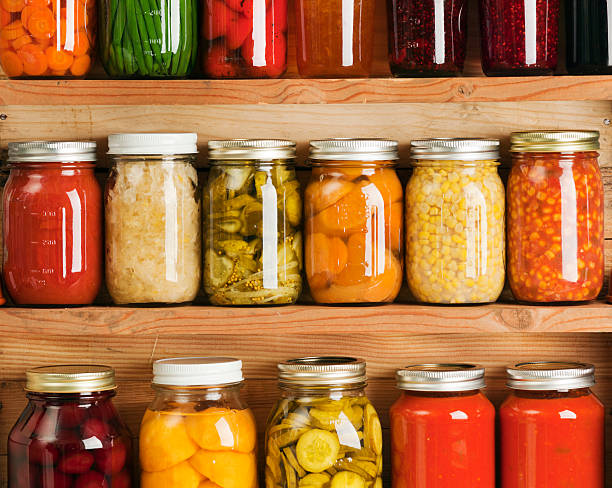 Home Canning Fruit and Vegetable Food Preserves in Storage Shelves Wooden storage shelves holding home canning vegetable and fruit preserves varieties, lined up in rows of glass jars. Canned food staple include jellies, sauces, carrot slices, green beans, tomatoes, corn, sweet potatoes, sauerkraut, roasted red peppers, dill pickles, red beets, peaches, rasperry jam, orange marmalade, grape jelly, tomato paste and corn soup. preserved stock pictures, royalty-free photos & images