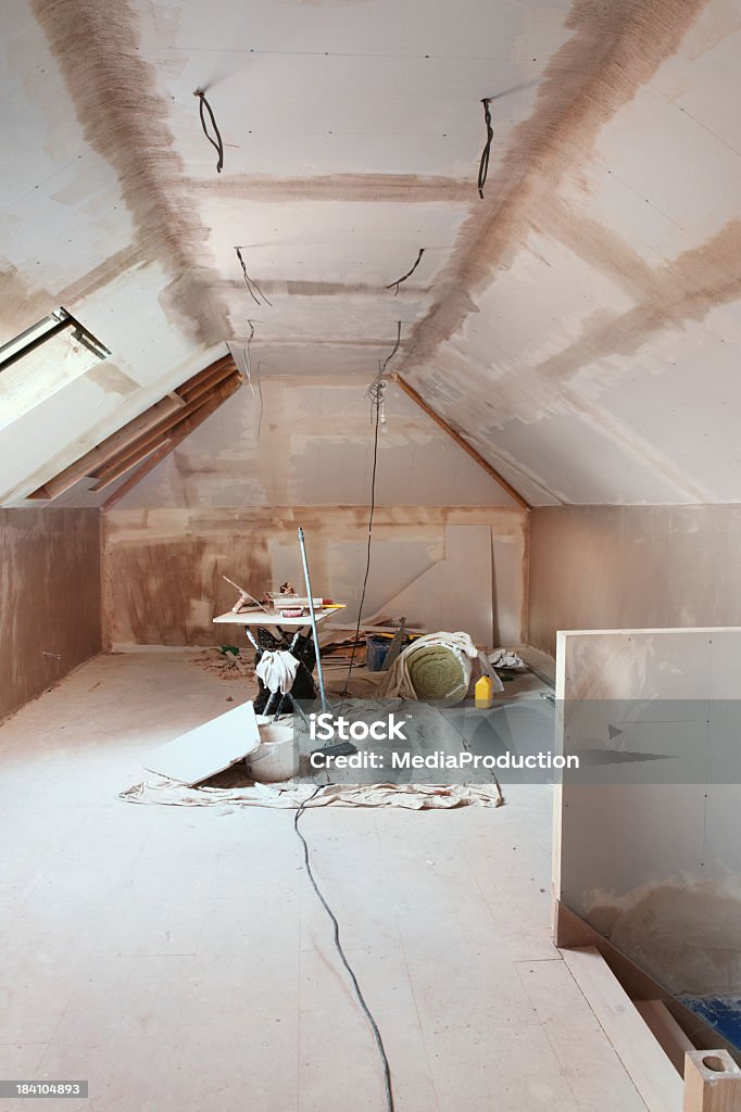 Attic conversion Attic conversion,, room with sloped ceiling,, semi-plastered,, plastering tools,, insulation,, ceiling light wires visible. Home Addition Stock Photo