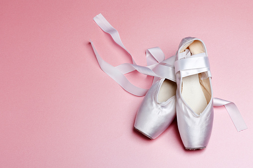 A pair of white pointe shoes on a pink background.