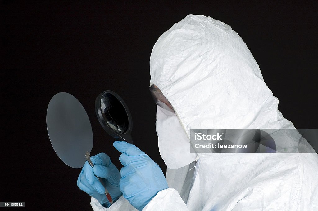 Inspecting a Silicon Wafer "Profile of a man in a hazmat protective suit and mask inspecting a silicon wafer with a magnifying glass.  Isolated on black.Click below for more in this series, plus all of my high-tech lab shots:" Computer Wafer Stock Photo