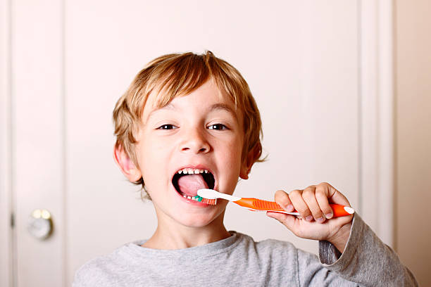Young boy brushing his teeth with orange toothbrush  stock photo