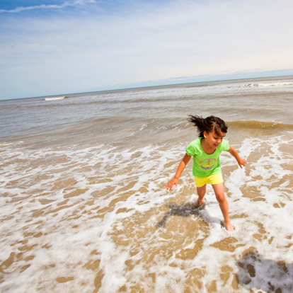 Little girl running and splashing in the water carrying a bucket.