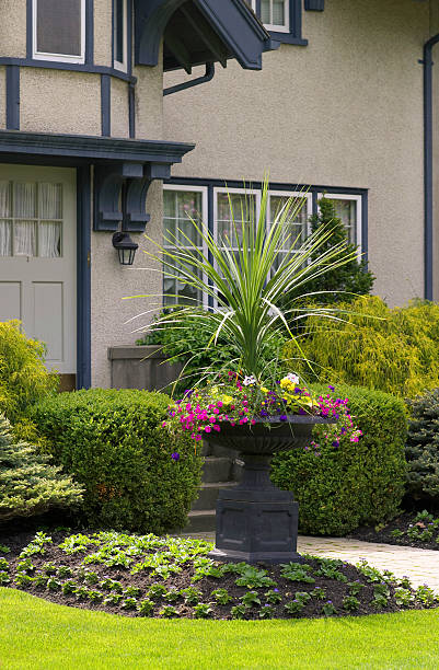 Purple flowers and a single pink tulip are blooming in an ornate stone urn, with a pond in the background