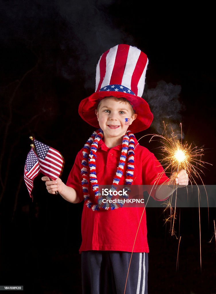 Patriotic Boy Holding Fourth Of July Sparkler & Flags Shown here is a four-year-old (4) boy proudly holding burning sparklers and American flags.  He is all decked out in patriotic garb and flag face paint. Vertical with Uncle Sam hat. 4-5 Years Stock Photo