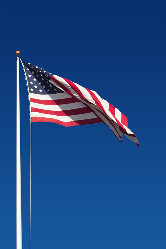 American Frag on a flagpole twirling and twisting in the wind against a deep blue clear sky. Horizontal view and copy and design space provided.