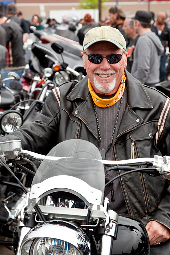 Motorcyclist at a biker rally in leather jacket  looking cool sitting on motorcycle and smiling looking into camera with crowd of bikers in background. Photo taken with Canon 5D Mark2 at 100 ISO, 24-115mm lens.
