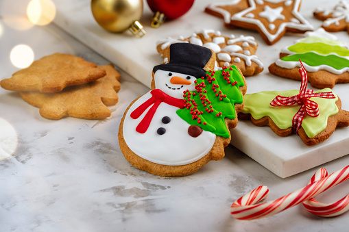 Homemade Christmas cookies decorated with icing on white background. Gingerbread cookie in the shape of snowman with Christmas tree and festive decorations. Concept of preparing Christmas cookies for the winter holidays.