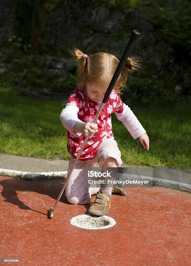 Menina jogando minigolfe de uma forma imparcial, sentando - Foto de stock de Buraco royalty-free