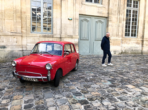 Paris, France: Man looks at a vintage red Autobianchi auto in the courtyard of the Picasso Museum. Designed to resemble the Fiat 500, the Italian car first appeared in 1957.