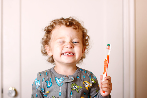 A three year old toddler in his pajamas brushing his teeth. Front tooth missing.