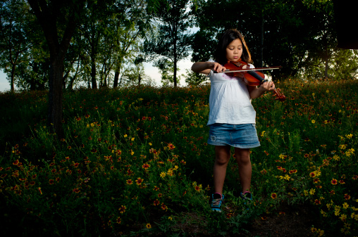Little girl playing violin in nature.