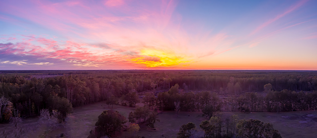 Aerial view of a beautiful Sunset with a bright orange sun, pink and purple clouds and a red hue over the treetops in Rural Texas
