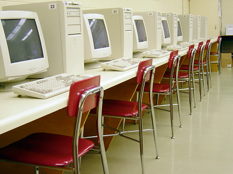 Row of numbered computers with red chairs.