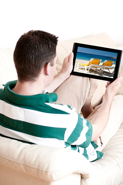 człowiek siedzi na kanapie za pomocą tabletu - digital tablet beach digital display pc zdjęcia i obrazy z banku zdjęć