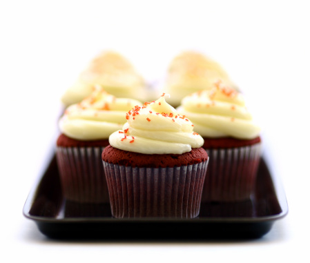 A closeup shot of four small cupcakes with cream and sprinkles on a white background