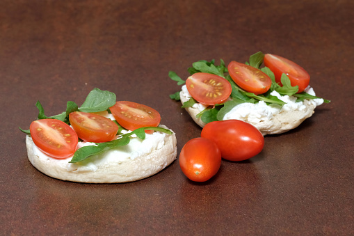 Ricotta cheese with cherry tomatoes and arugula on English muffins.