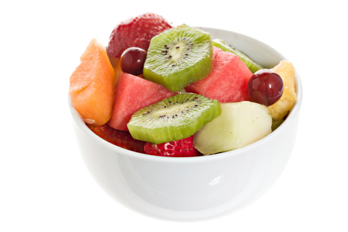 A close up overhead view of a colorful fruit salad in a white bowl. Isolated on white.