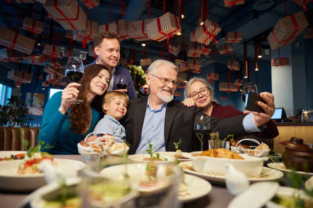 Delighted family celebrating New Year with festive dinner in cafe making selfie Delighted family celebrating New Year with festive dinner in cafe making selfie on smartphone for memory kids restaurant pictures stock pictures, royalty-free photos & images