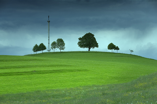 Mobile phone mast on a green hill against a threatening cloudy sky.
