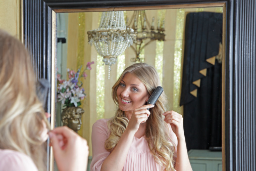 A beautiful women brushing her hair in front of an elegant mirror