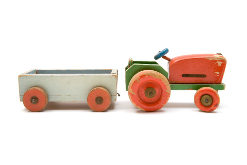 Run-down wooden toy tractor with trailer isolated on a white background.