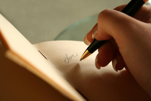 Love written on a leatherbound journal with fine paper pages.  Very shallow depth of field, focus on tip of pen.