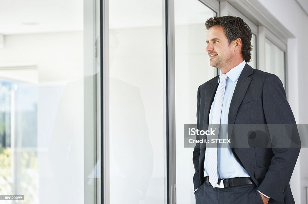 Executive looking out through a glass door Business man with hands in pockets looking out through a glass door 30-39 Years Stock Photo