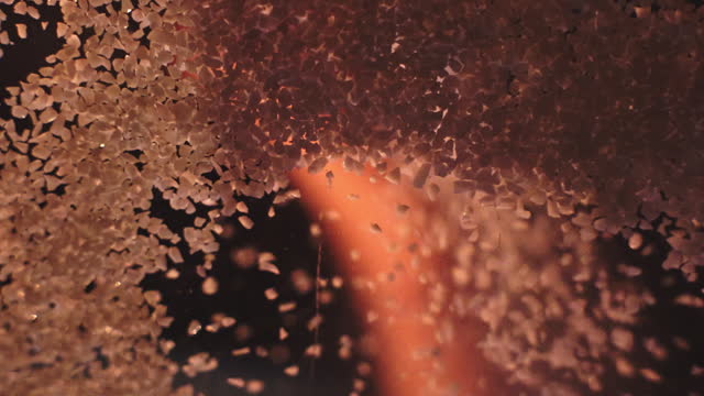 Human hand scattering a handful of glassblowing sand on the camera