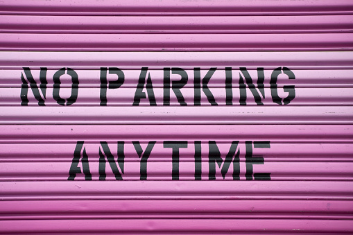 Clean black on pink No Parking Sign on steel door. Horizontal.