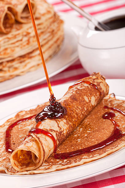 Chef pouring maple syrup over stacked pancakes with blueberries on top and cream on the side. Selective focus
