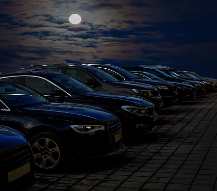 Cars in a parking lot at night in a row under the moon