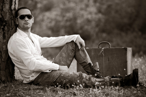 Man sitting with old-fashioned suitcase in the park.