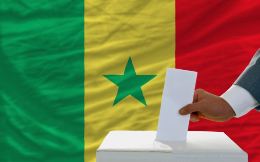 man putting ballot in a box during elections in senegal in front of flag