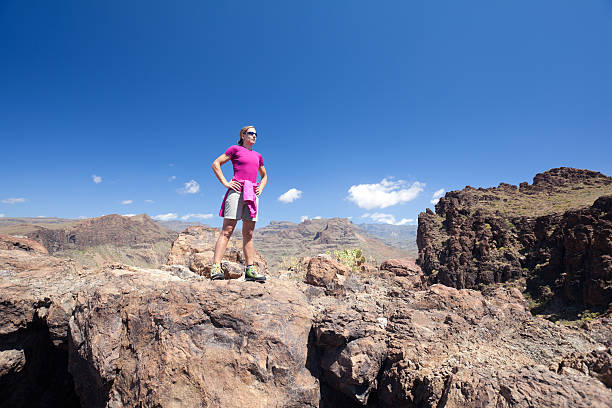 female hiker in colorful outfit standing on volcanic stones in rocky mountains with blue sky